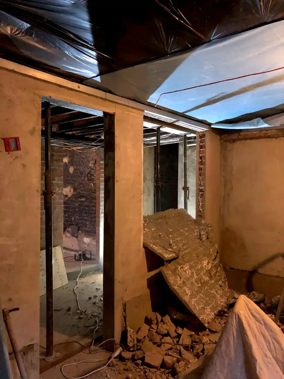 Structural prep stage in a London basement: exposed brickwork, fresh plaster on side walls and a new opening framed with steel