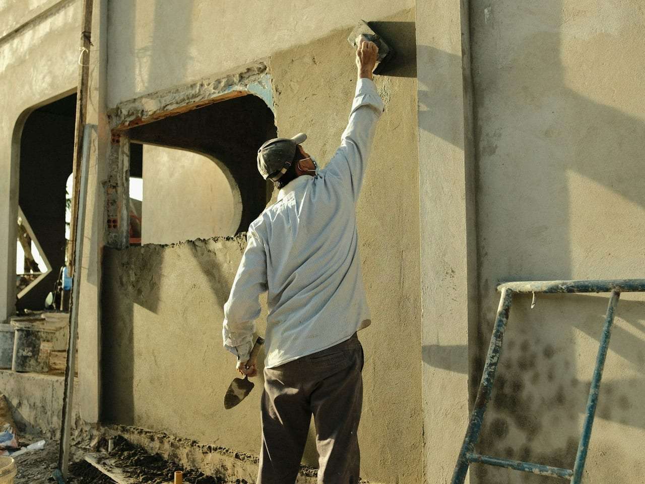 Plasterer applying a smooth coat of plaster around a window reveal with a trowel, in bright directional sunlight