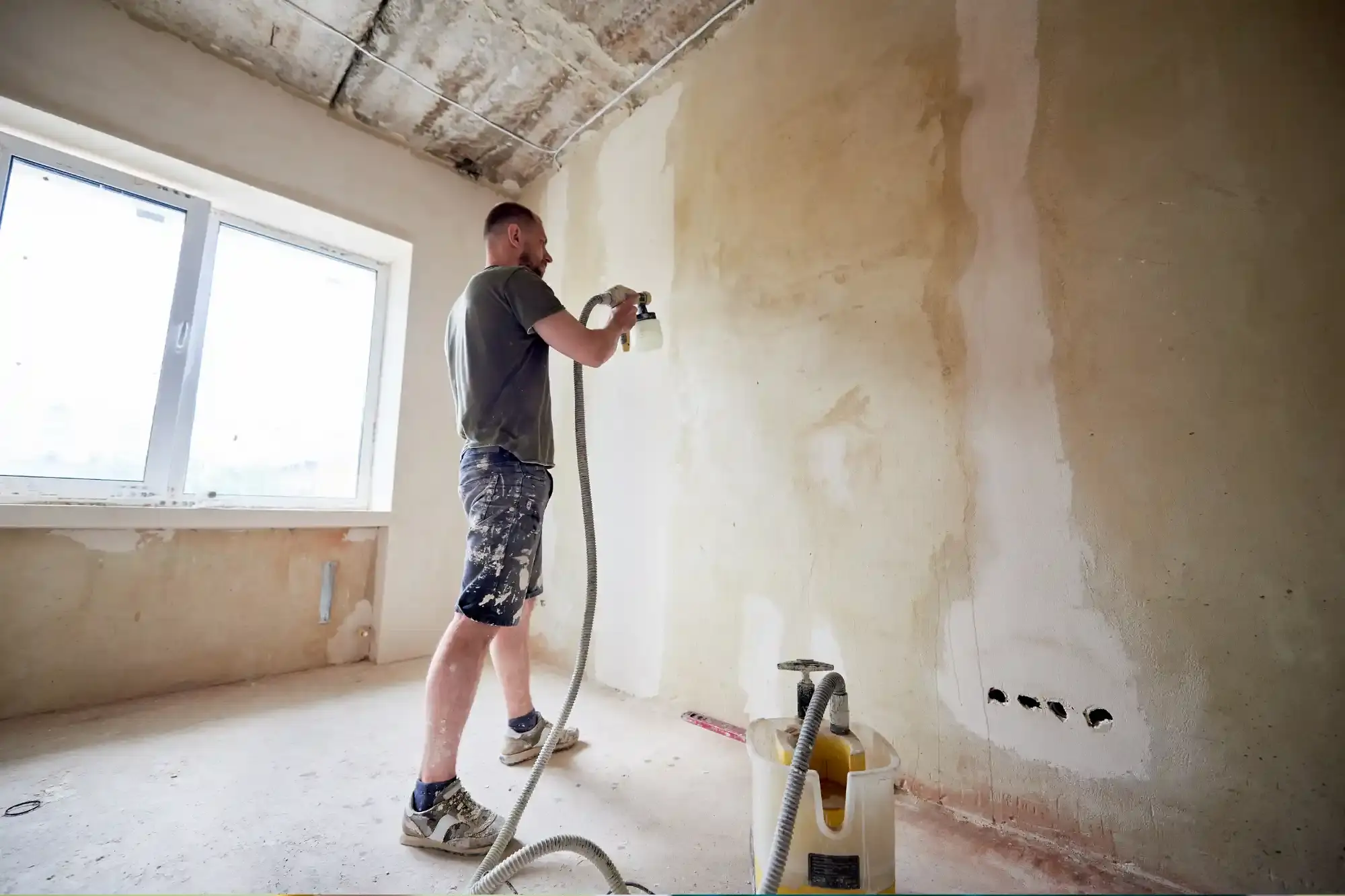 Decorator using a low-pressure spray gun to apply paint to an interior wall in a London property
